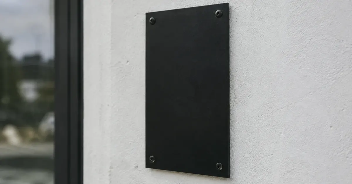 Plaque métallique noire vissée verticalement sur un mur blanc
